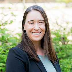 Outdoor headshot of Jessica, wearing a suit and smiling at the camera.