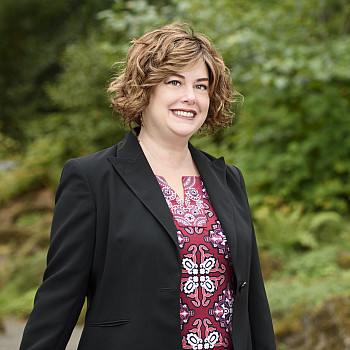 Cari posing outside, wearing a black blazer over a colorful top.