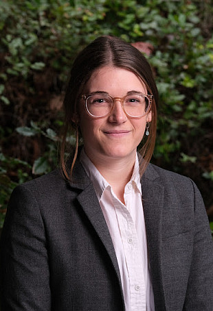 Maggie smiling at the camera, wearing a blazer and glasses.