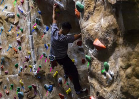 A student climbs on an indoor rock wall with ropes and harness