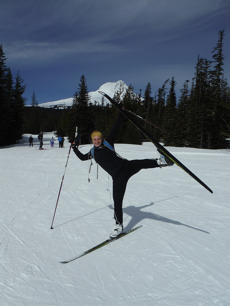 Gillian, a skate ski instructor puts her leg in the air while on a skate ski clinic posing and smiling in front of Mt. Hood.