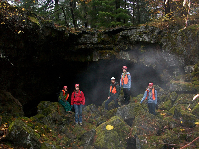 five students underground in a dark cave with hi vis orange vests and headlamps