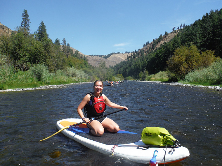 a person kneels on a SUP on a lake