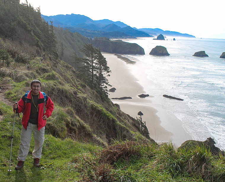 a person in a red jacket stands atop a bluff overlooking the ocean