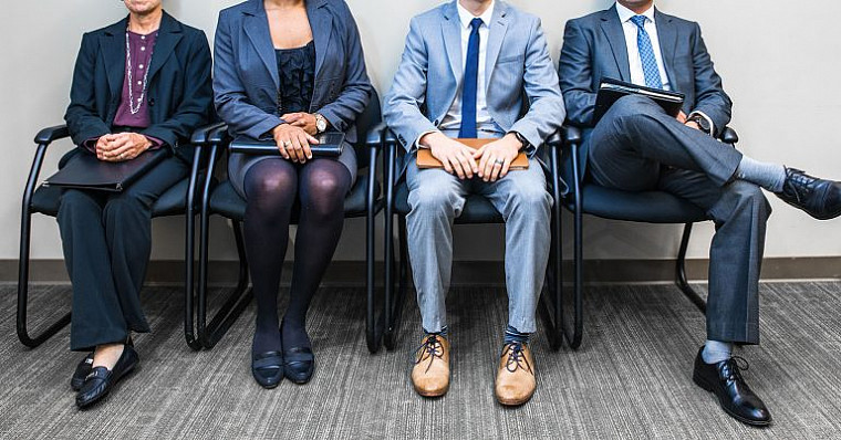 A variety of applicants are sitting in chairs, ready and waiting to interview.