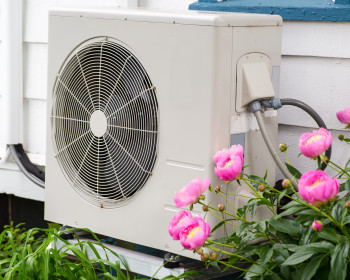 Air conditioning/ Heat pump unit on the side of a home among the flowers.