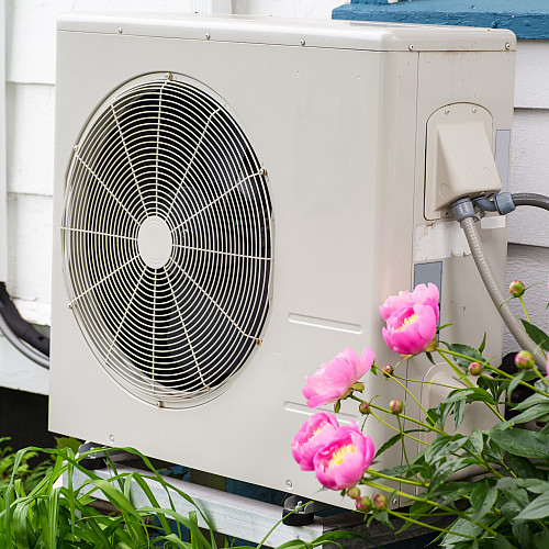 Air conditioning/ Heat pump unit on the side of a home among the flowers.