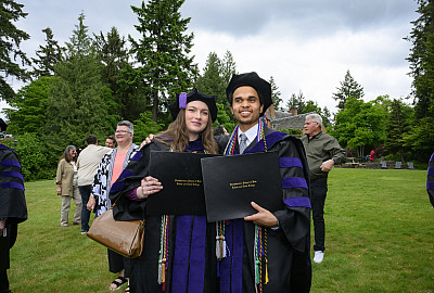 Two graduates holding up their diplomas outside.