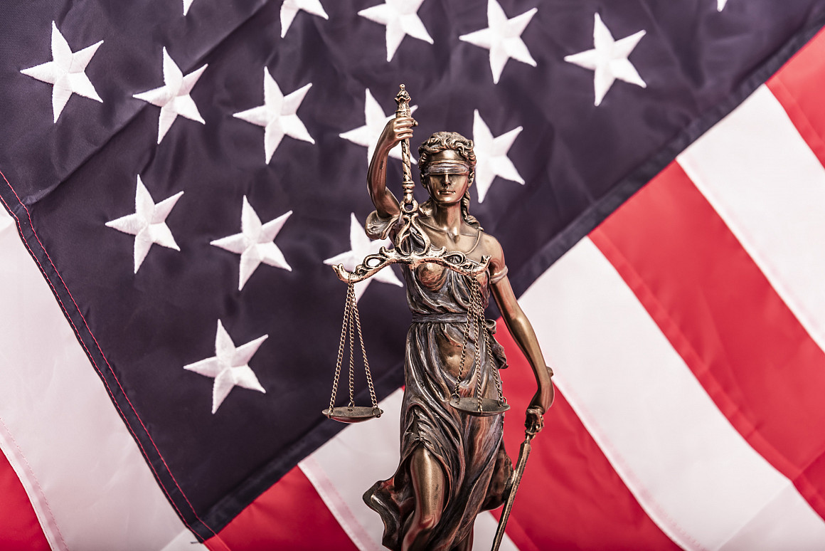 The statue of justice Themis or Iustitia, the blindfolded goddess of justice against a flag of the United States of America, as a legal c...
