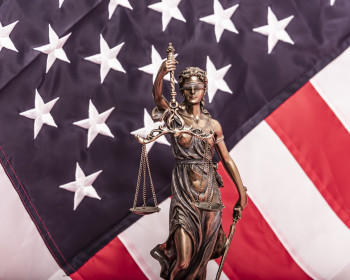The statue of justice Themis or Iustitia, the blindfolded goddess of justice against a flag of the United States of America, as a legal c...