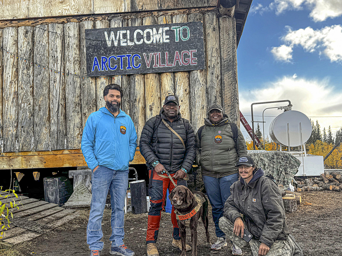 A group stands under the Arctic Village sign.