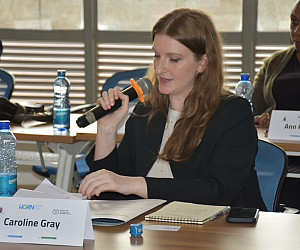 Caroline sitting a table speaking into a microphone.