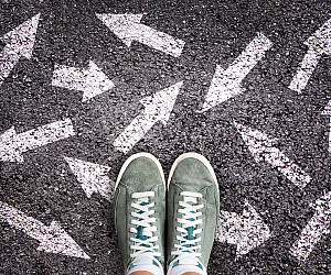Sneaker shoes and arrows pointing in different directions on asphalt ground, choice concept