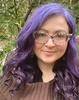 JaDee is smiling at the camera with trees and plants in the background 